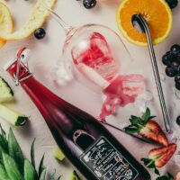 flat-lay photograph of sliced fruits, swing top bottle, and wine glass